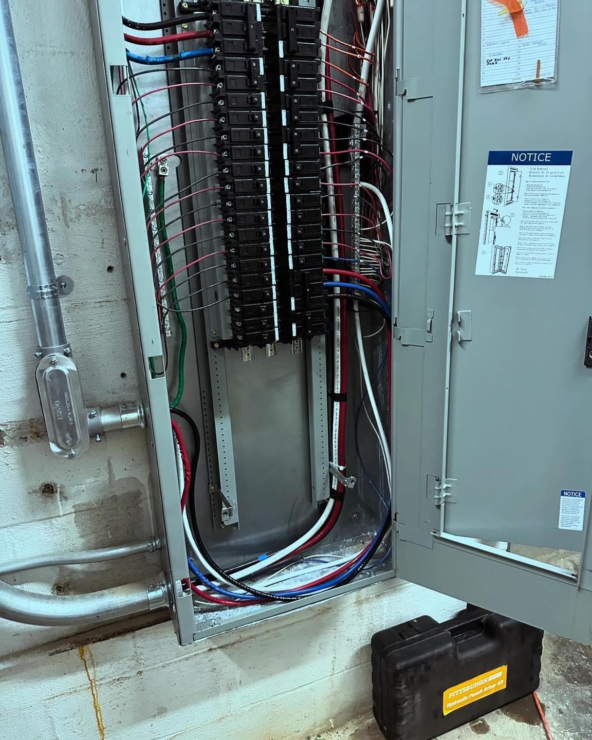 Open electrical panel with wires; a black toolbox rests on the floor.