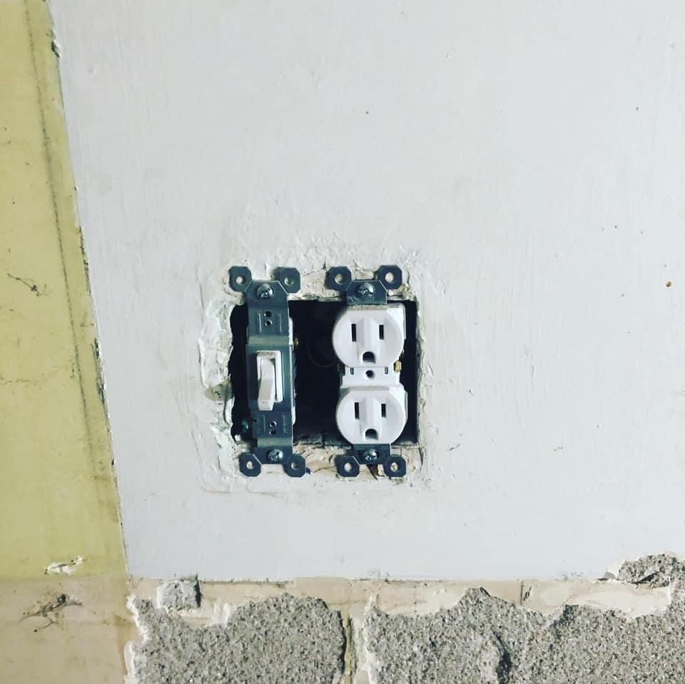 Light switch and electrical outlet installed in a rough opening in a white wall.