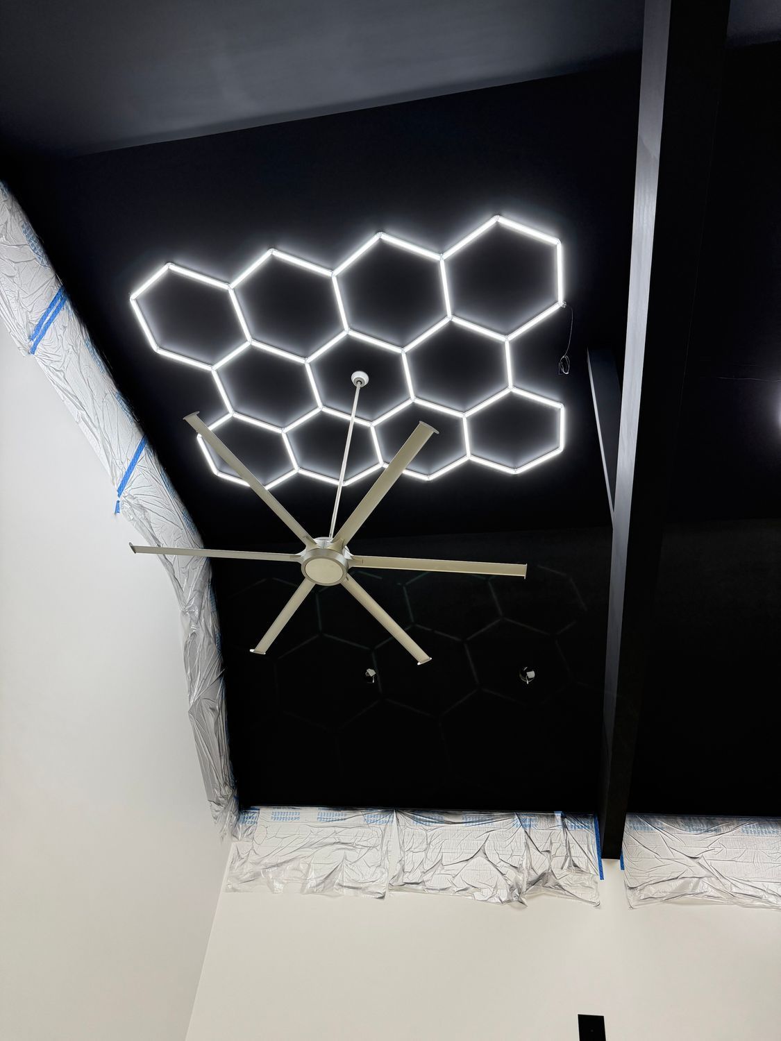 Black ceiling with white hexagonal lights, a ceiling fan, and white walls.