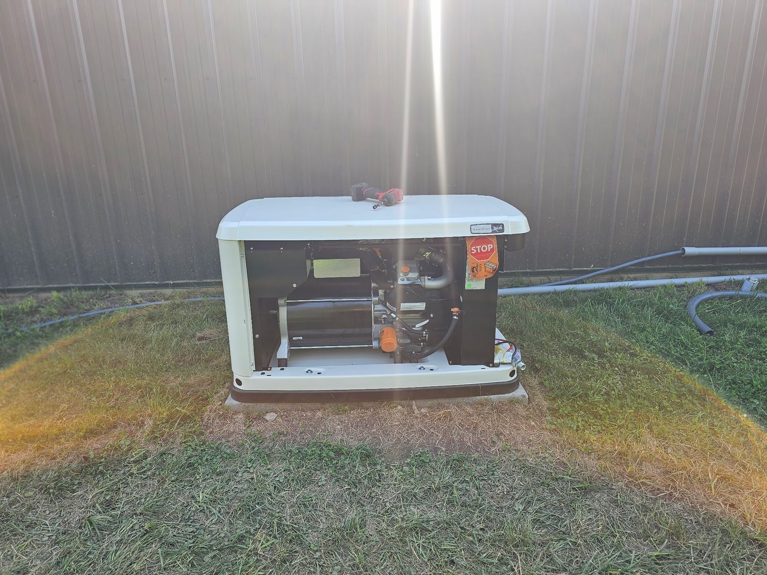 Generator on a concrete base in a grassy yard, near a brown fence, with bright sunlight.