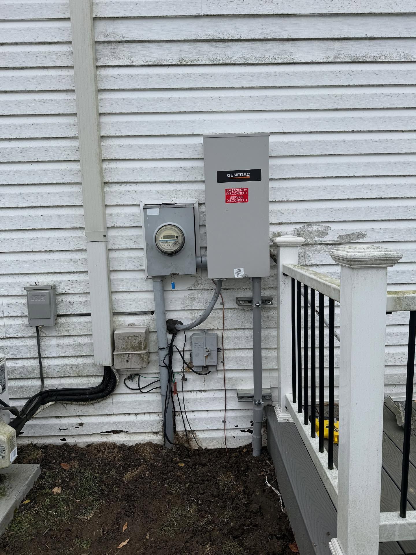 Exterior electrical panel and meter box on white siding next to a deck with black railing. Gray conduit and wiring.