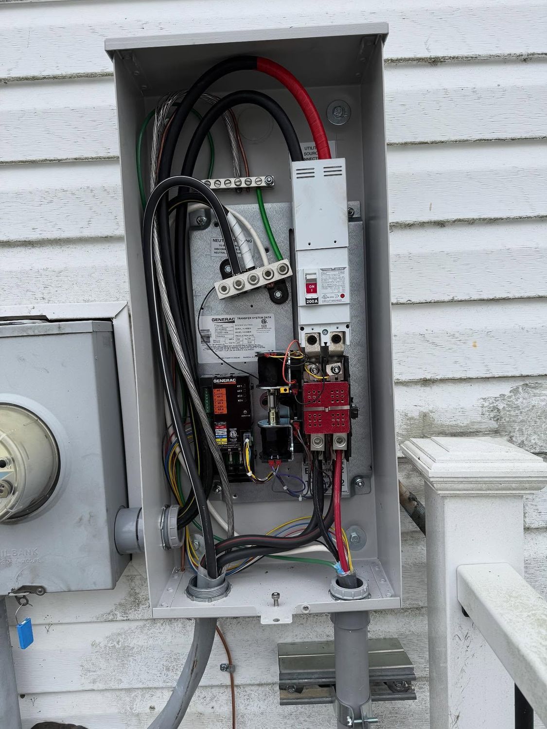 Open electrical panel on a building exterior with wires and components visible. Grey, black, and red wires are present.