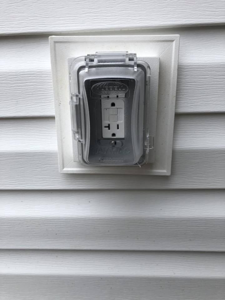 Exterior electrical outlet with gray weatherproof cover on white siding.