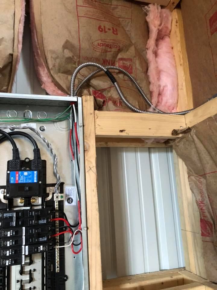Electrical panel with wiring, insulation, and metal siding visible in a wall.
