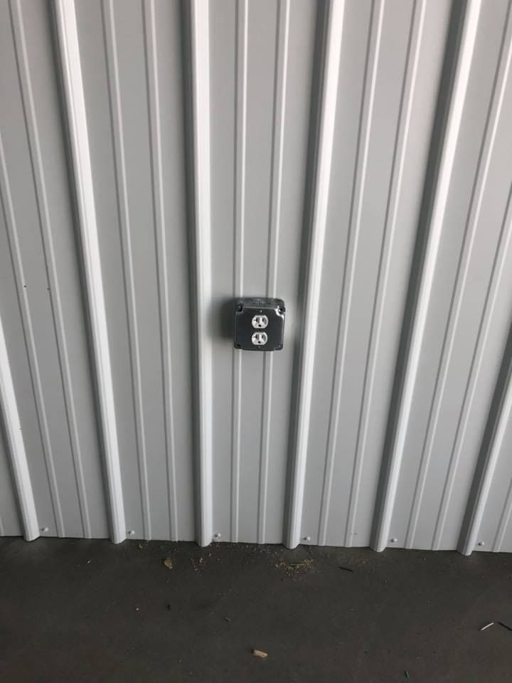 Gray electrical outlet on a corrugated white metal wall.