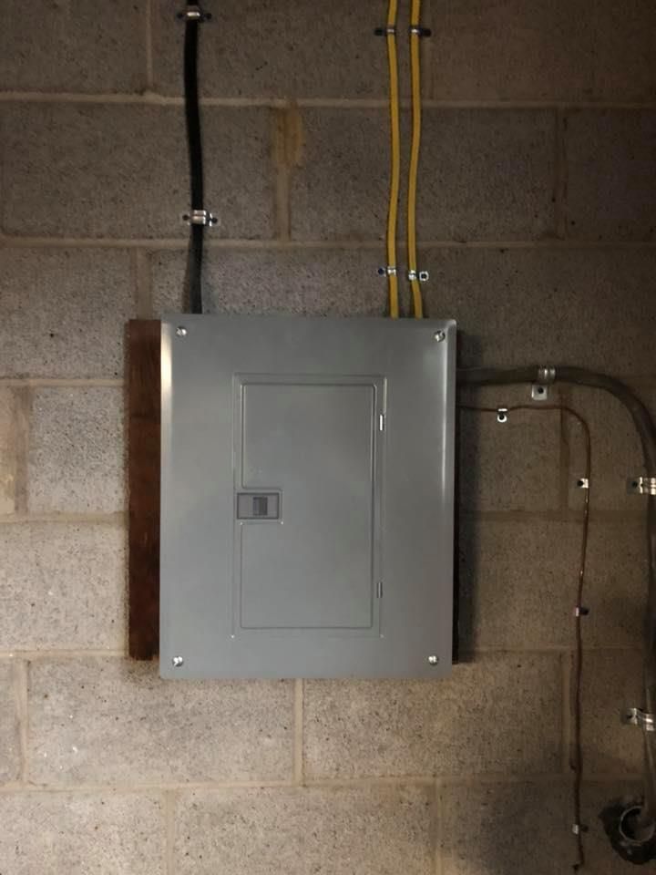Electrical panel mounted on a cinder block wall, with conduits and cables attached.