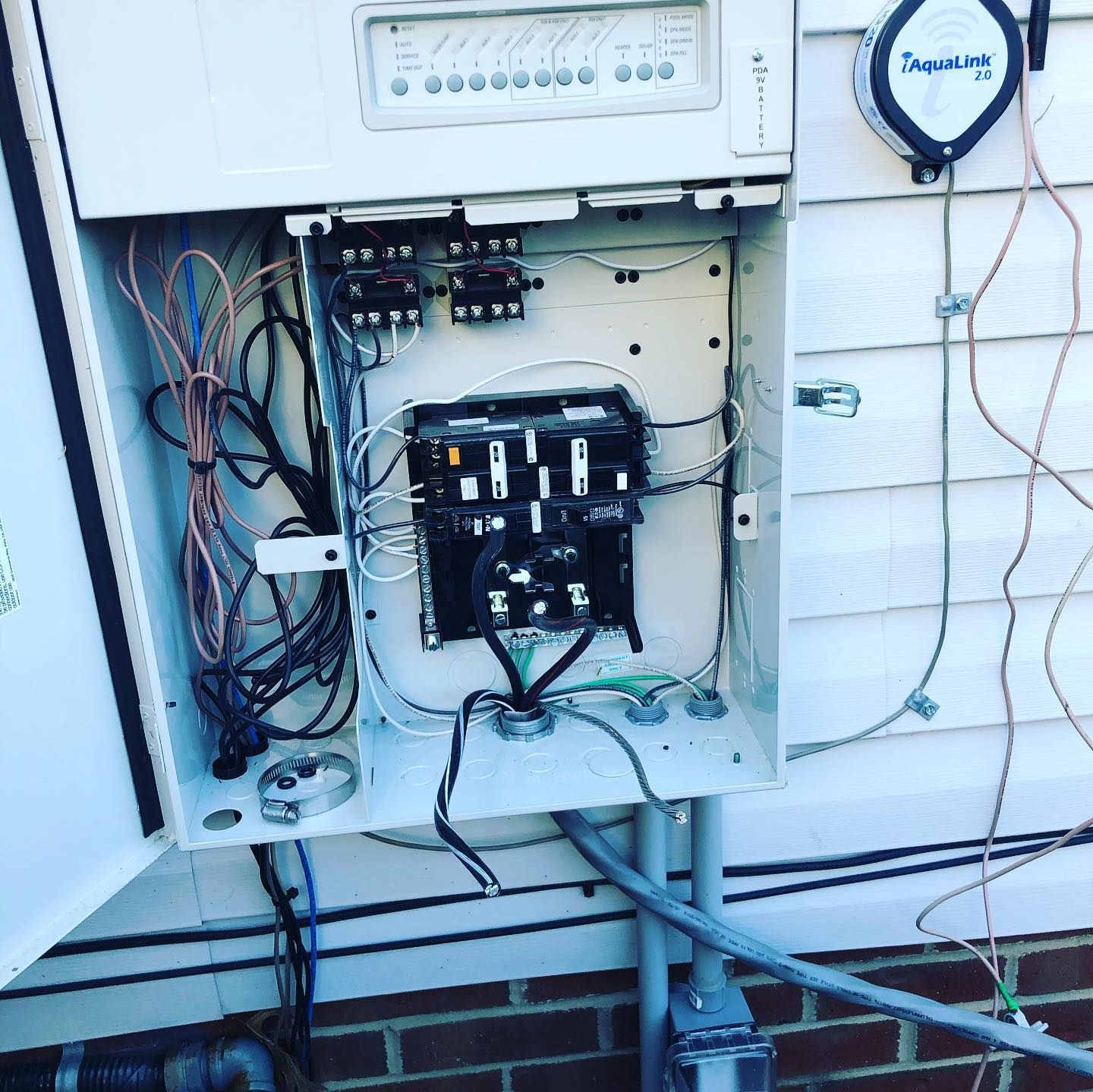 Open electrical control box on a white house exterior with wires and components visible.