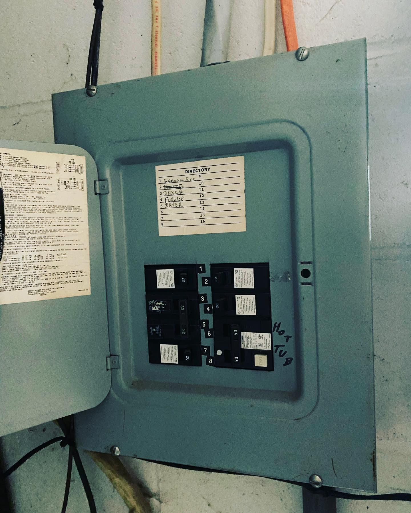 Open, gray electrical breaker box with visible breakers and labels on a wall.