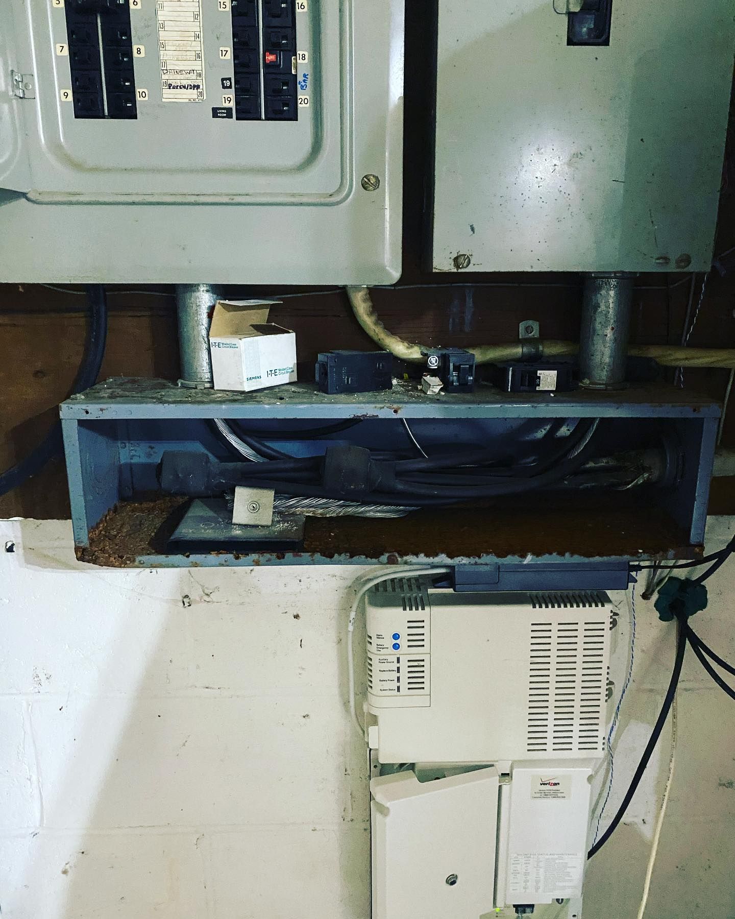 Electrical panel and wiring in a basement, gray metal, dusty with some exposed wires and components.