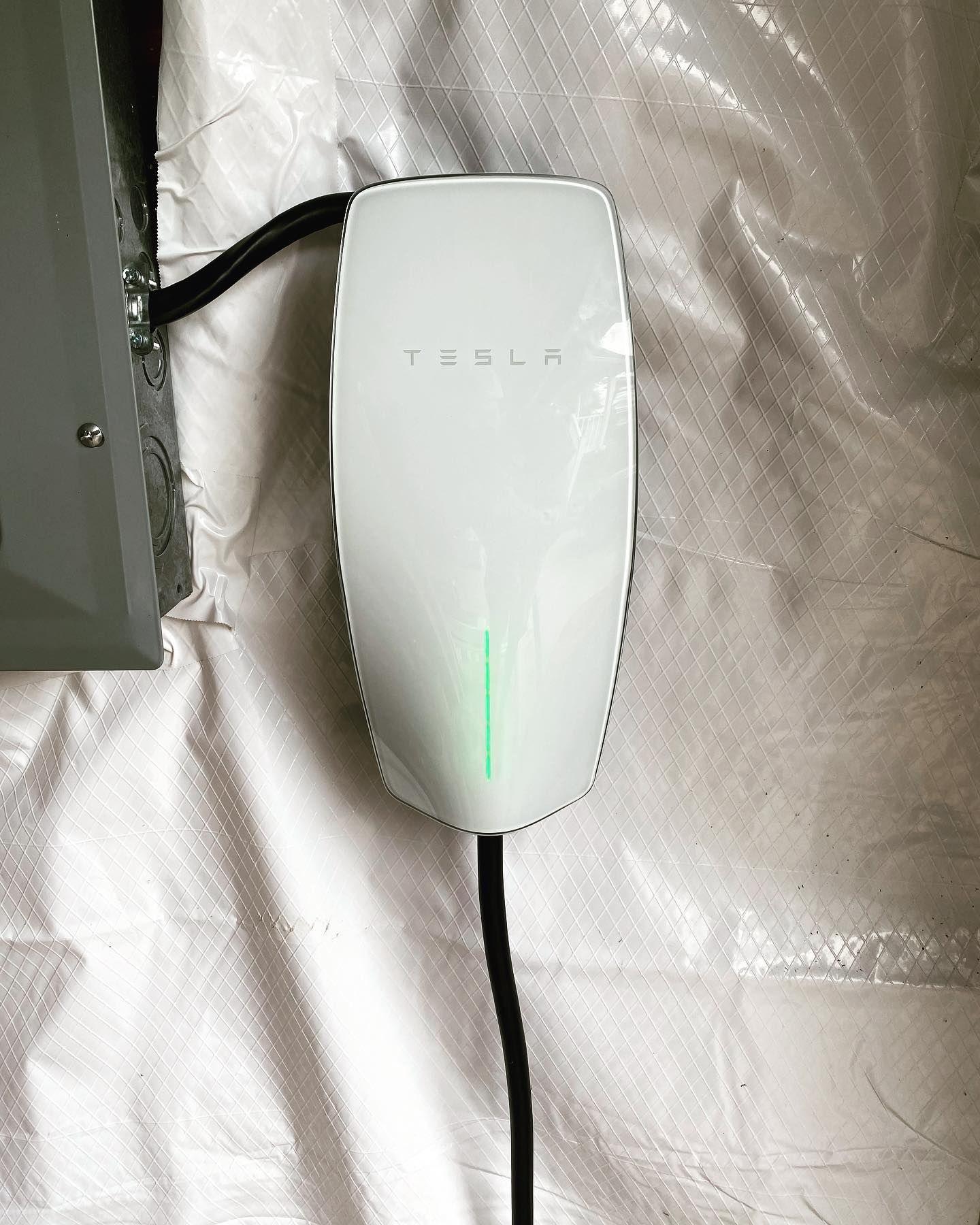 White Tesla wall charger with a green light installed on a white wall.