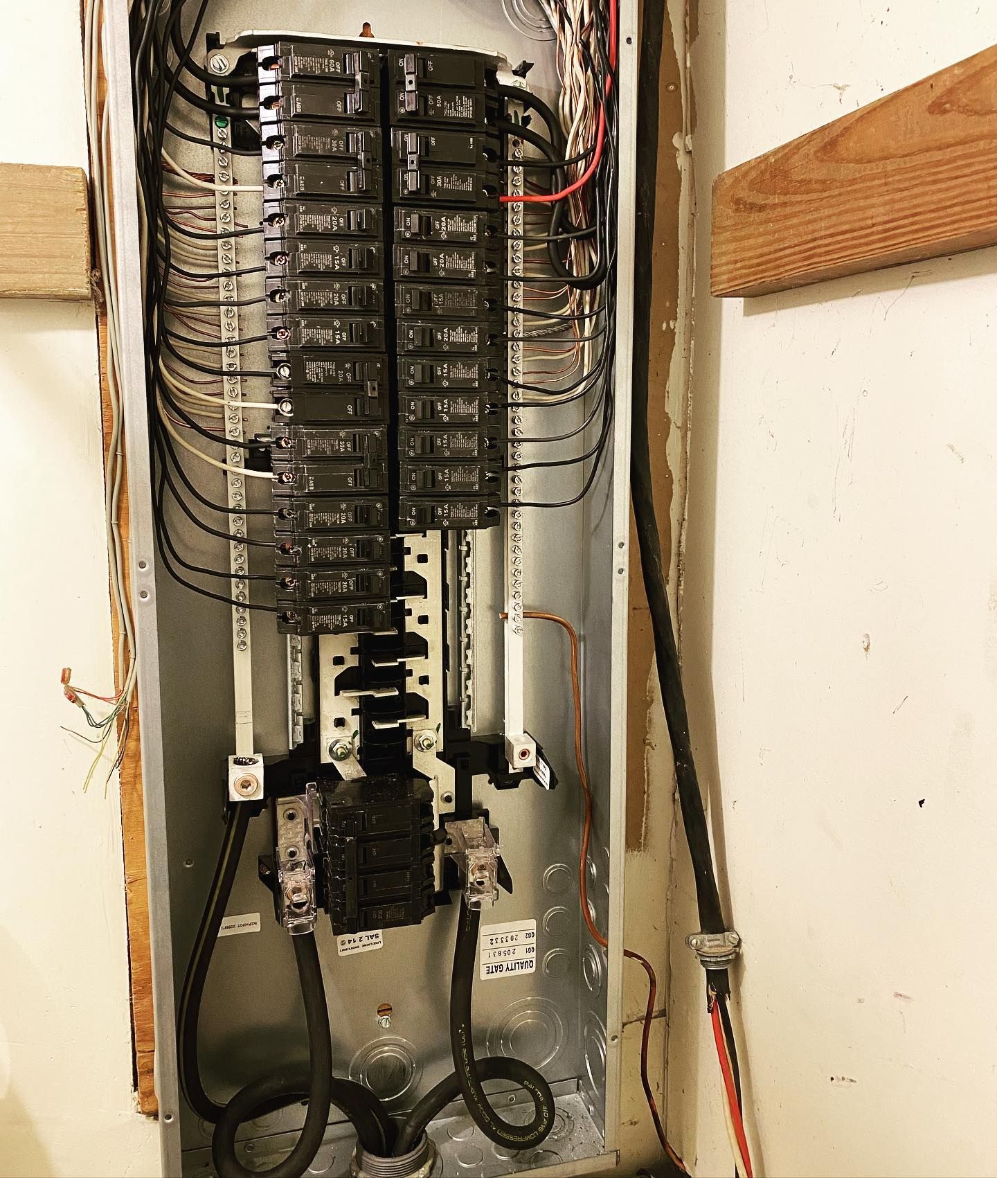 Open electrical panel with black breakers and wires in a wall.