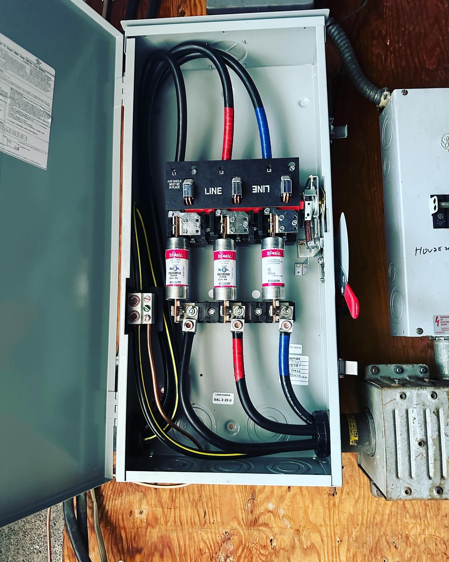 Electrical fuse box with black, red, and blue wires, and three red cylindrical fuses.