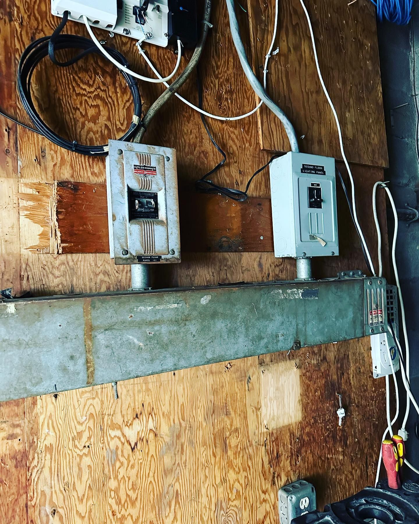 Two electrical boxes mounted on a wooden wall with wires and conduit, and a metal beam below them.