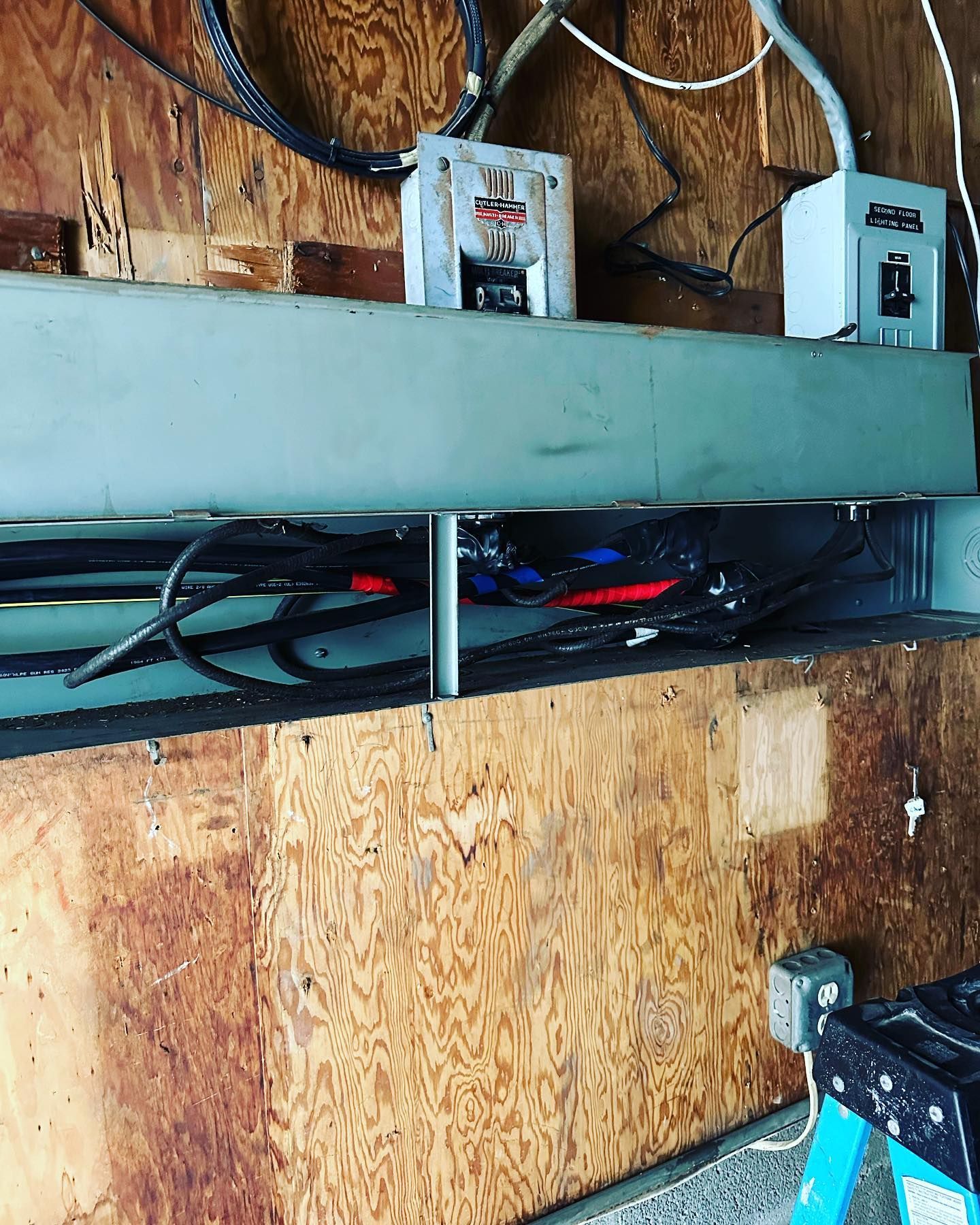 Electrical panel on a wood wall with exposed wires and conduit.