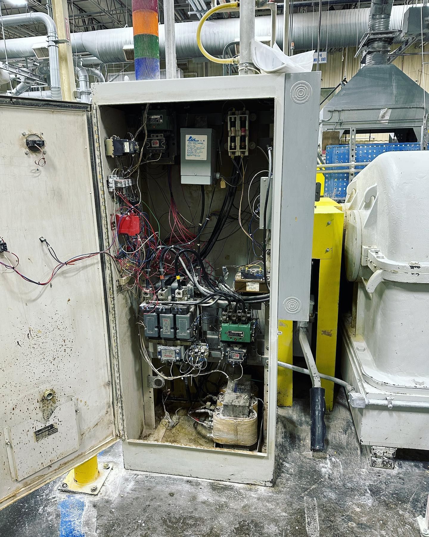 Open electrical panel with exposed wires and components in a factory setting, with a stack light on top.