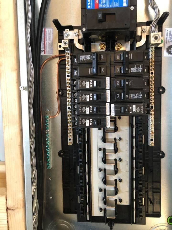 Electrical panel with breakers and bus bars, mounted on wooden studs. Ground wire attached to a ground bar.