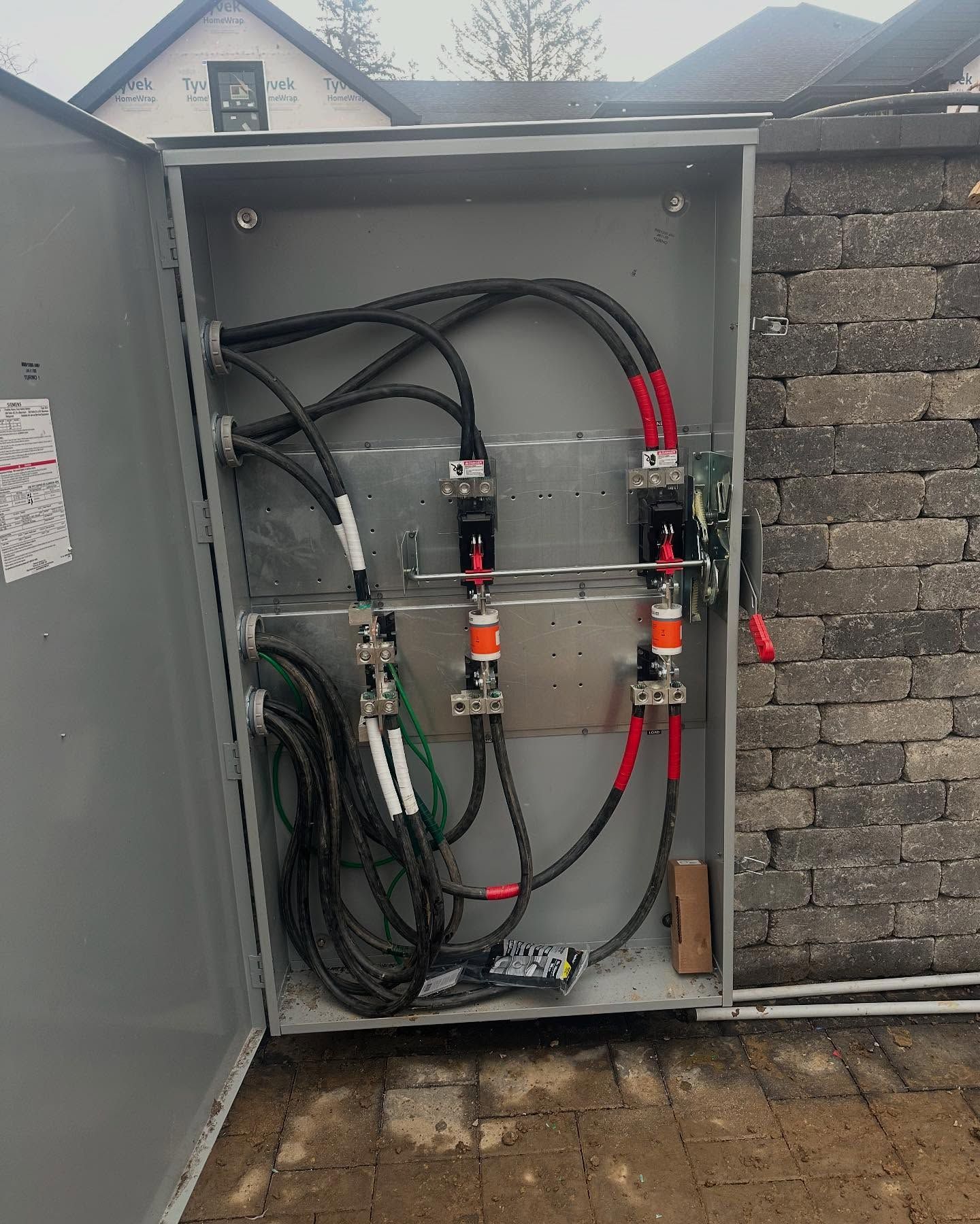 Open metal electrical panel with black and red wires, mounted on a brick wall.