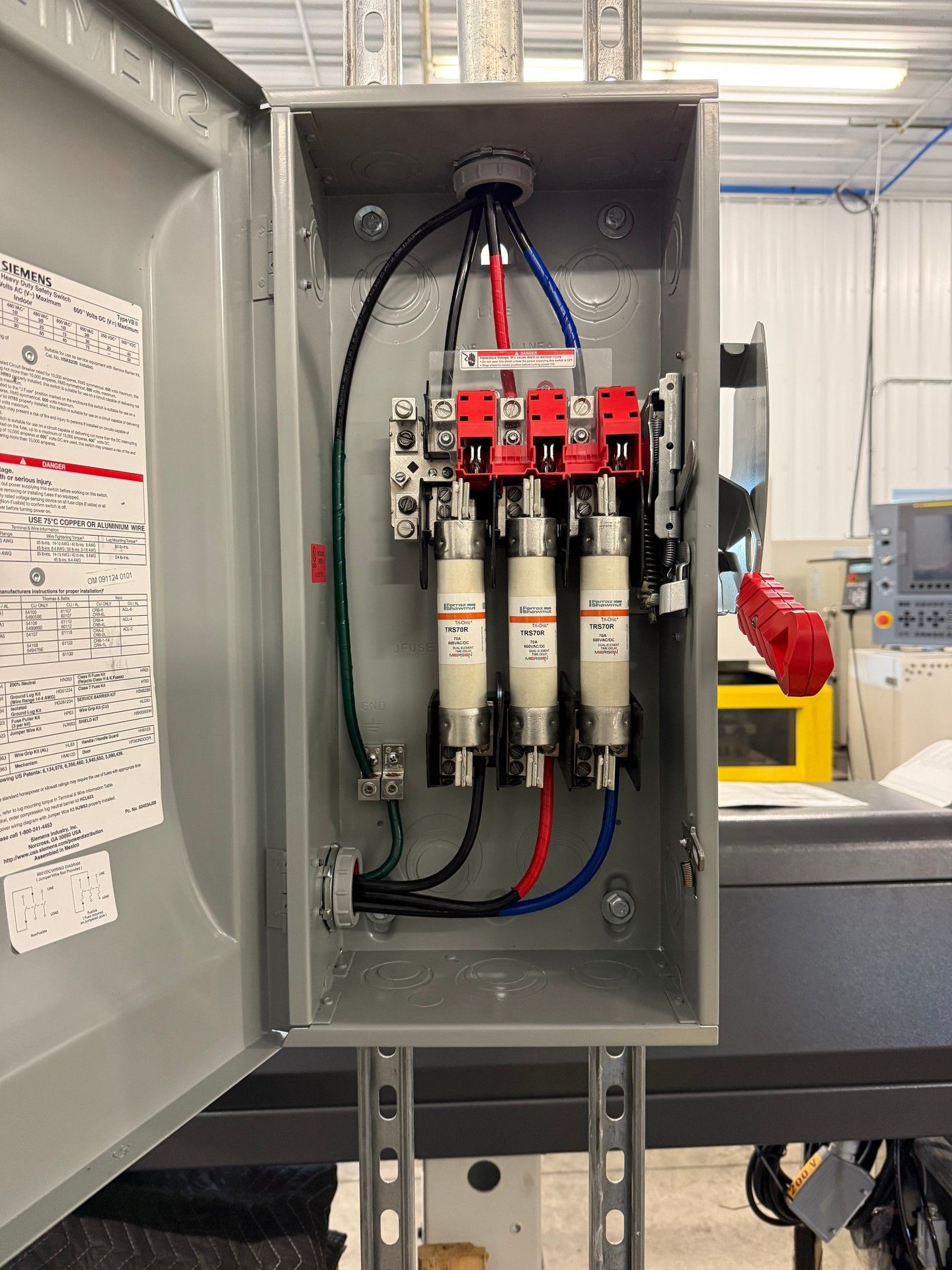 Electrical box with three cylindrical fuses, mounted inside a gray metal enclosure. Black, blue,  red wires are connected.
