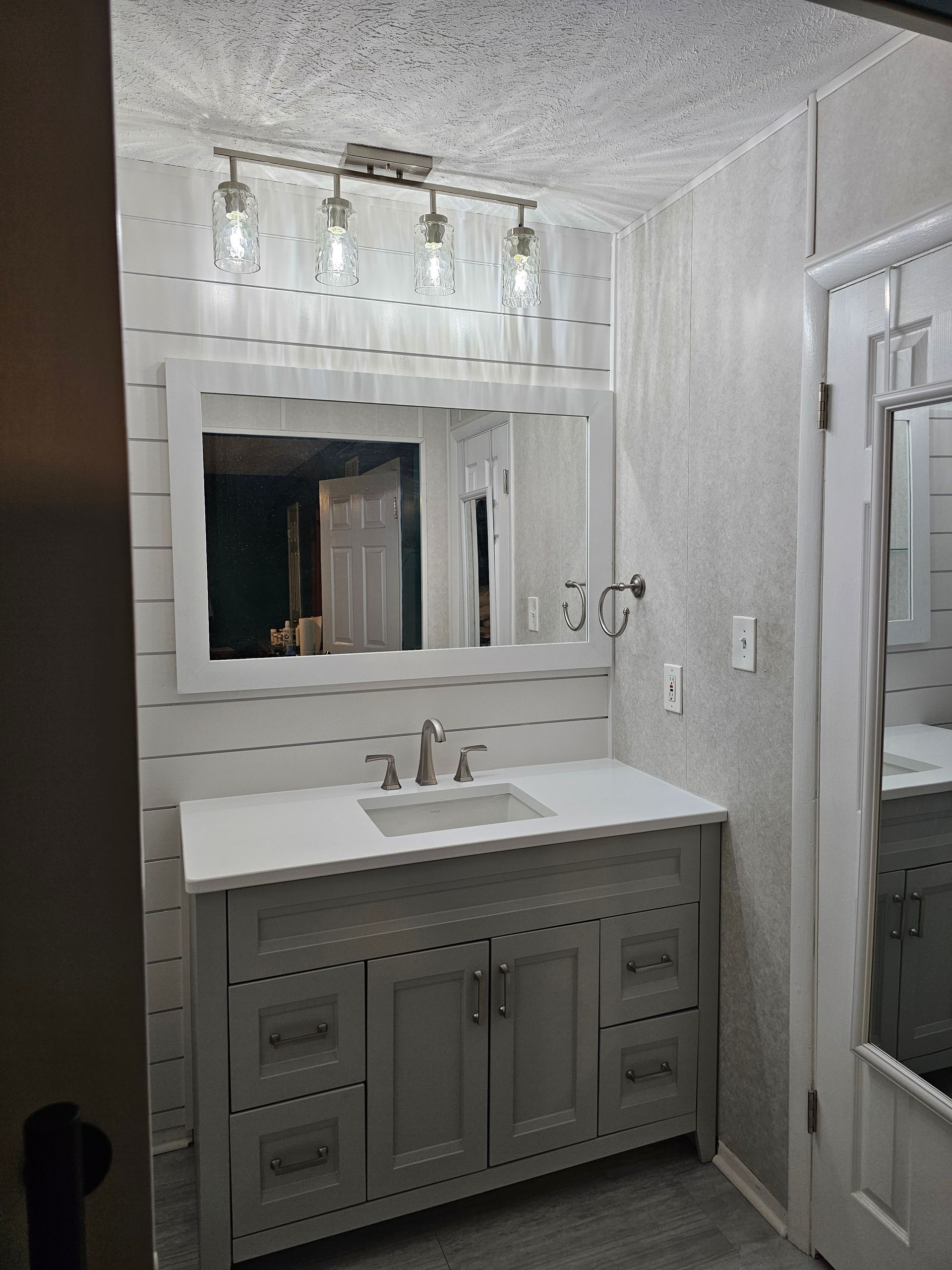 Bathroom with gray vanity, white countertop, large mirror, and four-bulb light fixture.
