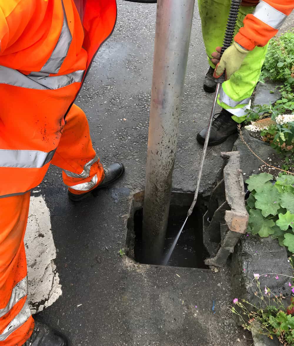 A Man In Orange Safety Pants Is Cleaning A Hole In The Ground — Gillen Plumbing In Ciccone, NT