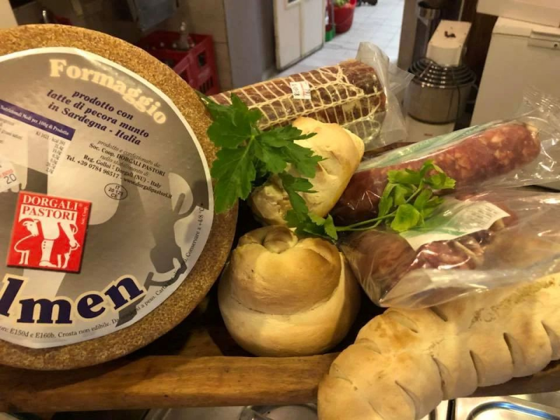 Forme di formaggio, salumi e pane disposti su un tagliere di legno.
