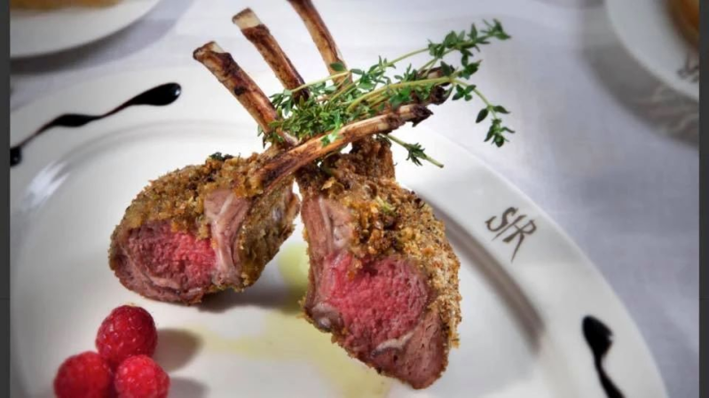 Due costolette di agnello impanate su un piatto bianco con rametti di timo e lamponi.