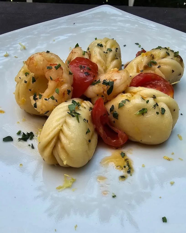 Gnocchi con pomodori, erbe aromatiche e scorza di limone su un piatto bianco.