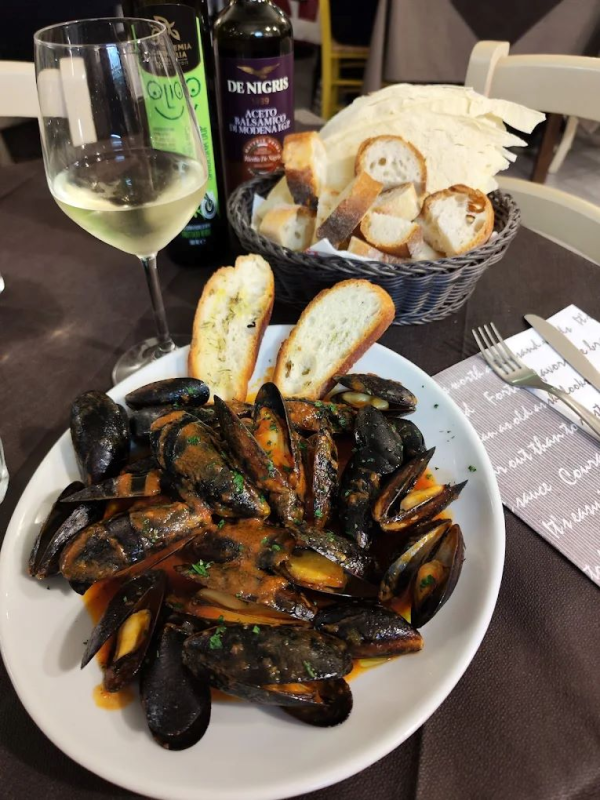 Cozze al vapore in salsa di pomodoro, cestino di pane, vino bianco. Apparecchiatura del tavolo del ristorante.