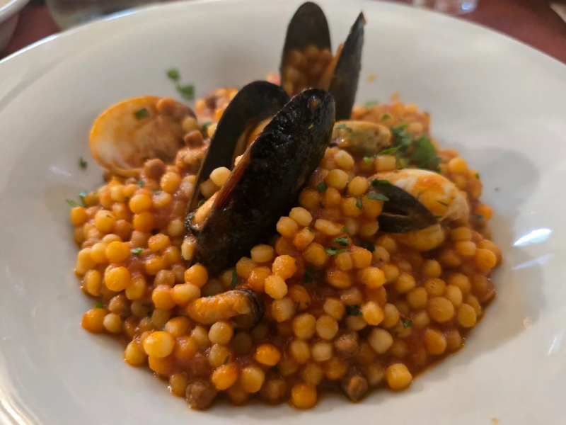Piatto di frutti di mare con cozze, couscous e salsa di pomodoro in una ciotola bianca.
