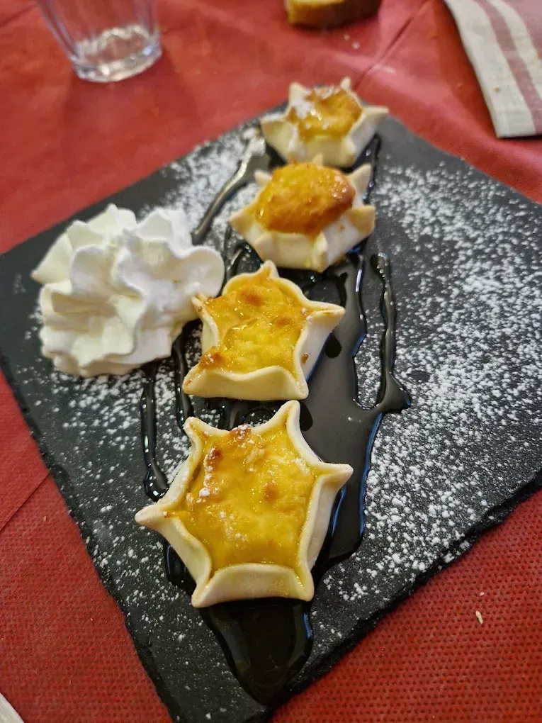 Pasticcini a forma di stella con ripieno di crema, glassa di cioccolato, panna montata e zucchero a velo su una lavagna nera.