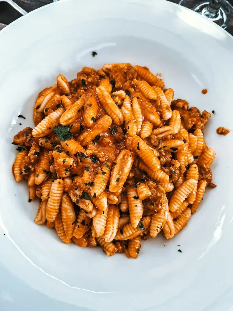 Primo piano di un piatto di pasta in una ciotola bianca, con salsa rossa e carne.