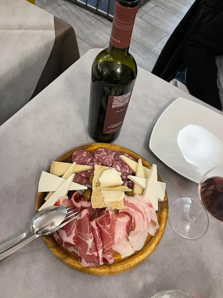 Tagliere di salumi con bottiglia di vino e bicchieri su un tavolo di un ristorante.
