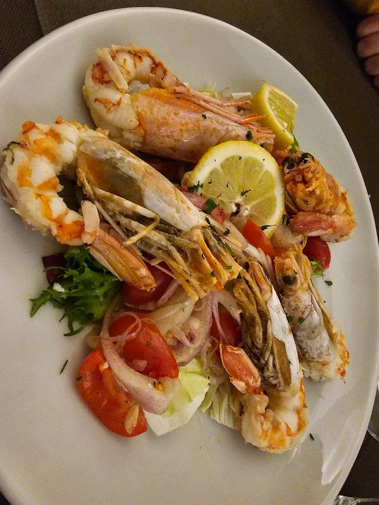 Gamberi e scampi cotti con fette di limone, insalata e pomodori su un piatto bianco.
