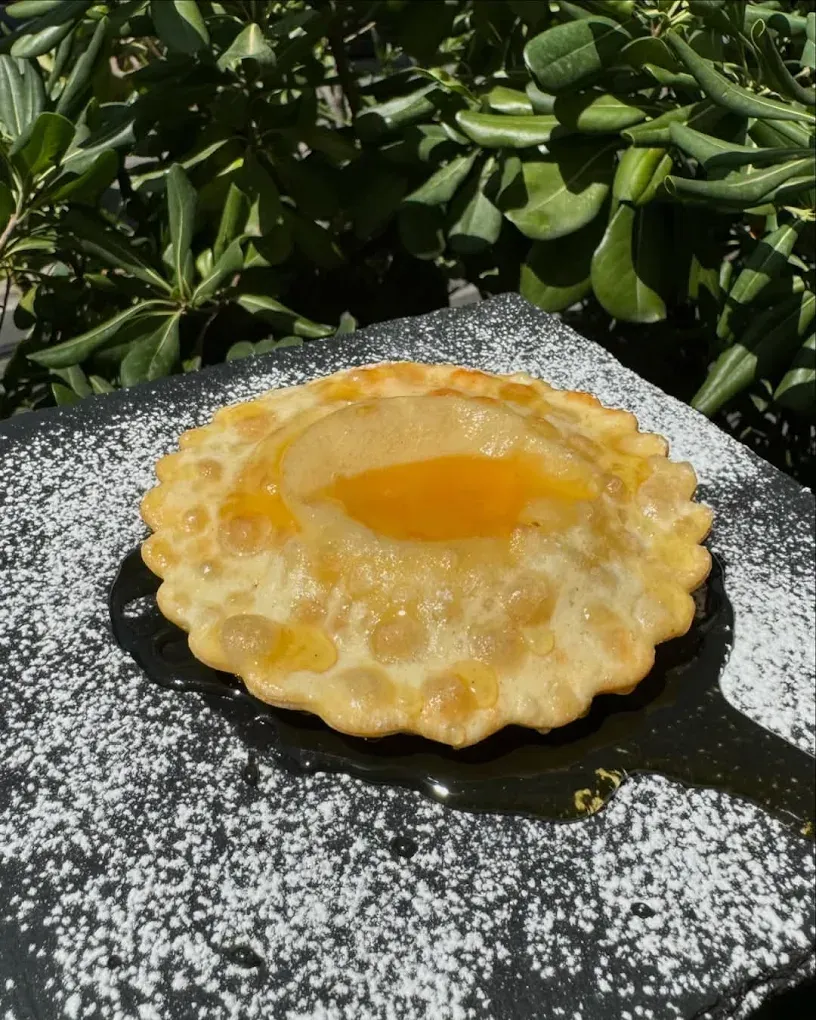 Pasta fritta con una fetta di pesca, miele a filo e zucchero a velo su una lavagna nera.