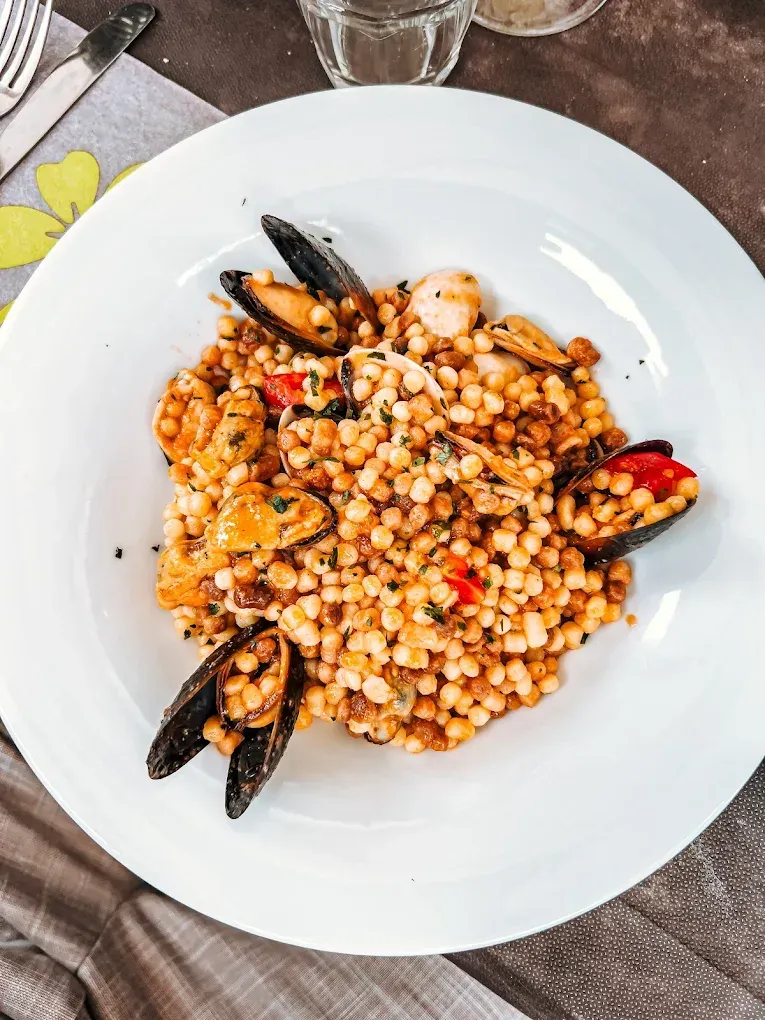 Piatto di frutti di mare su piatto bianco: cozze, couscous, salsa bruna.