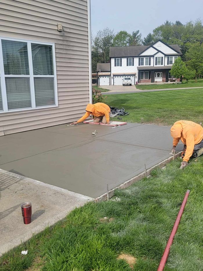 A man is spreading concrete on a sidewalk with a rake.