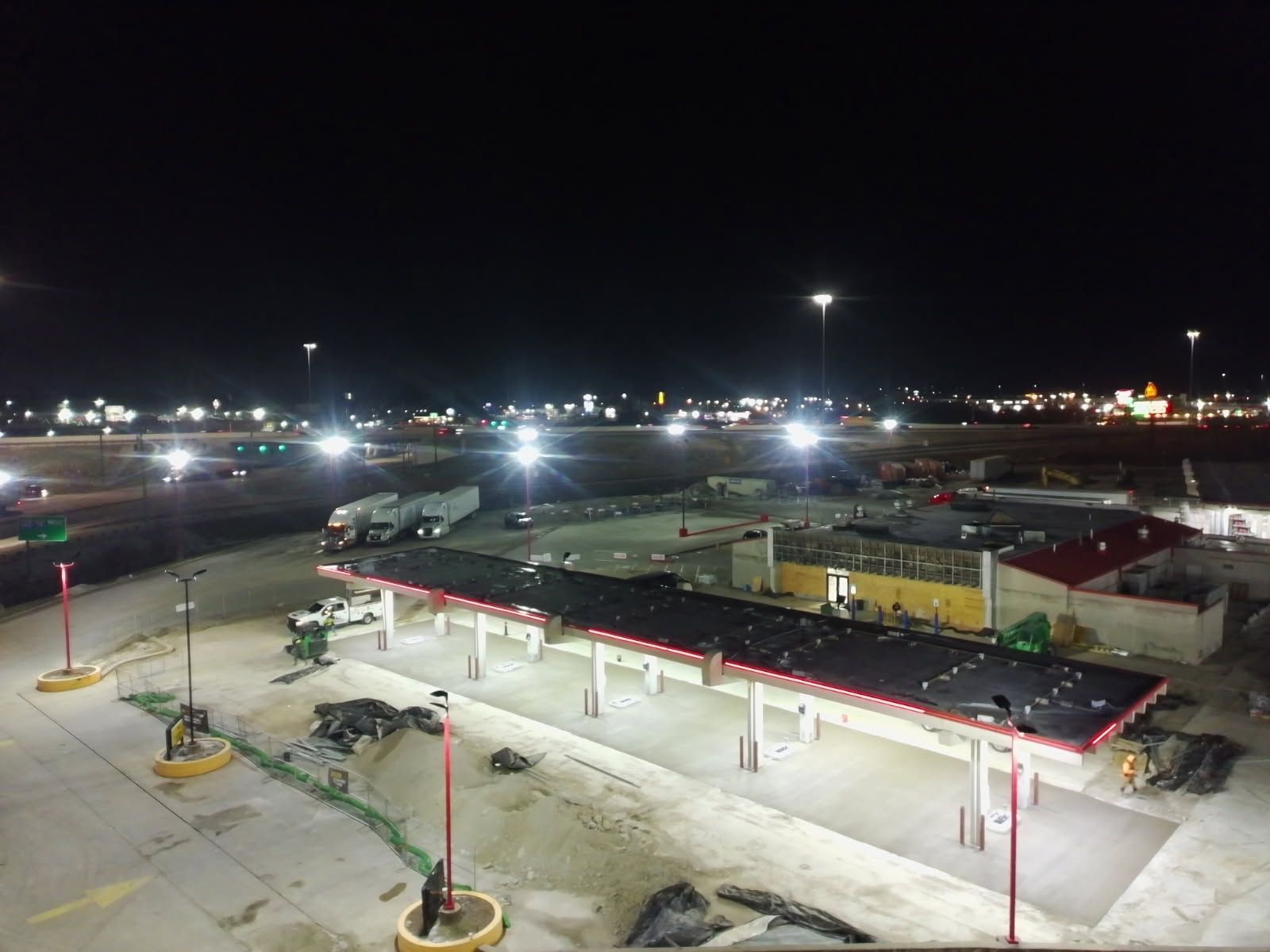 Gas station at night, with bright lights illuminating the building and surrounding area. Semi-trucks visible.