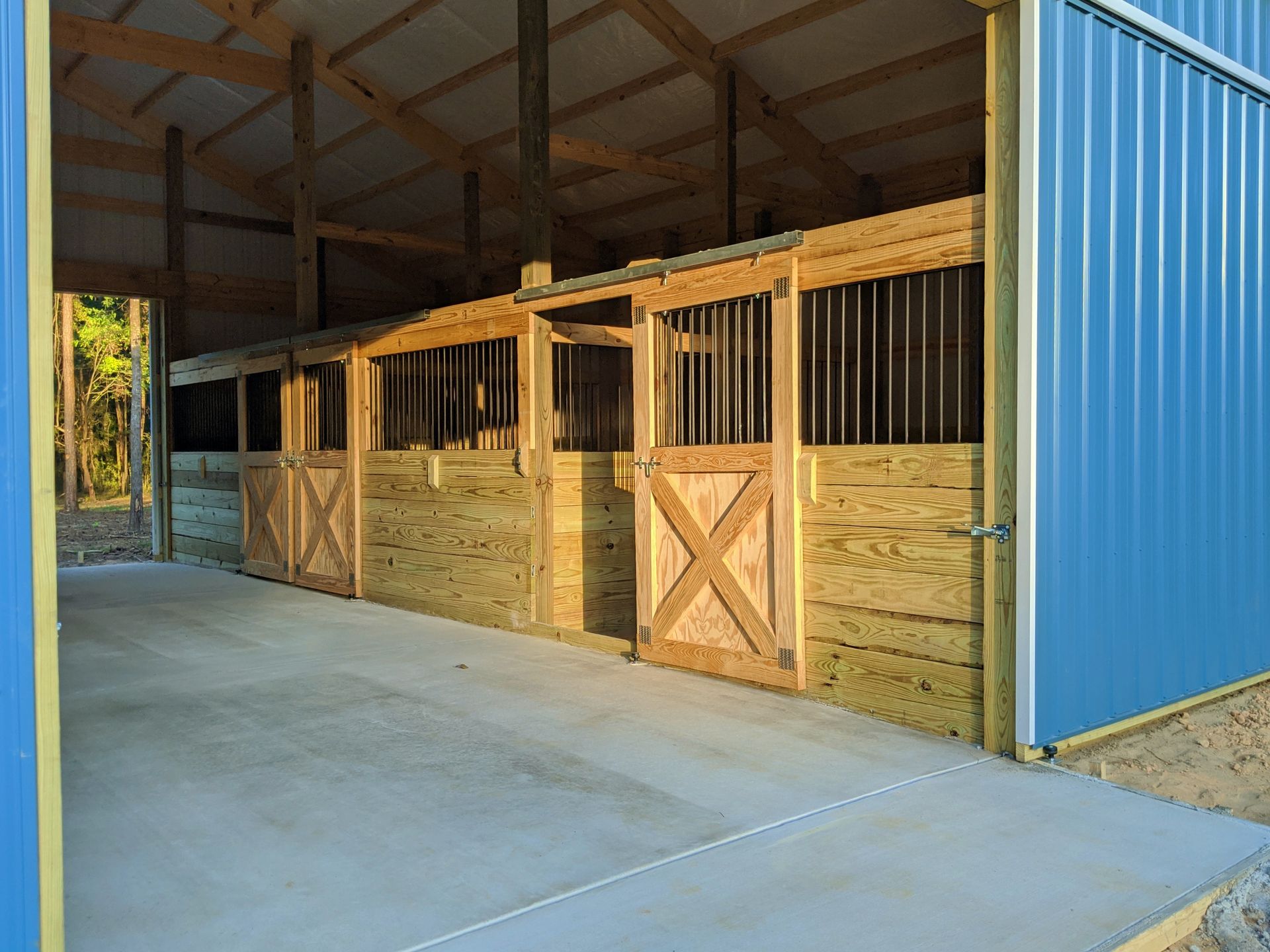 A pole barn with wooden stalls and a blue door.