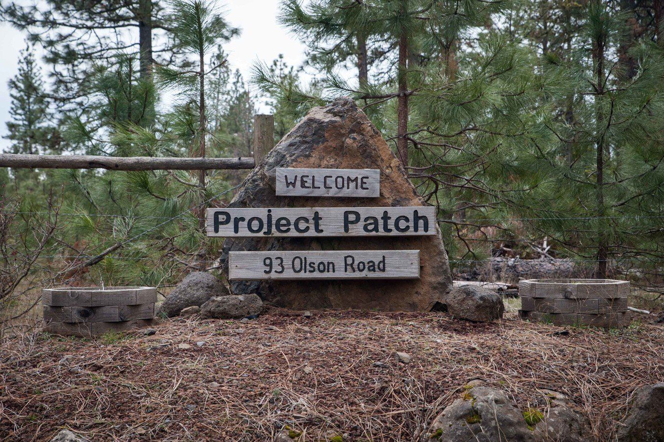 A large rock in the middle of a forest with a sign that says welcome project patch 93 olson road.
