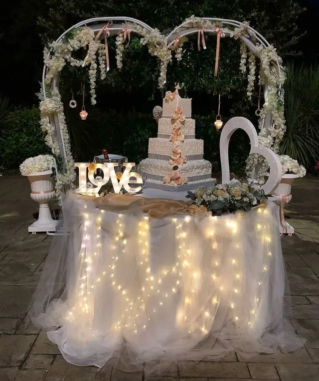 Una torta nuziale bianca a quattro piani su un tavolo decorato con lucine