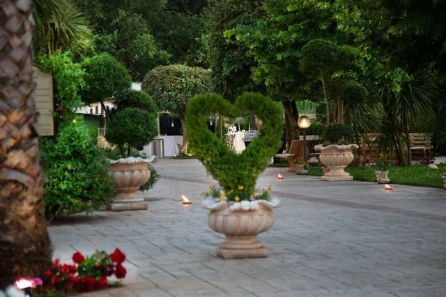 Un sentiero nel giardino è caratterizzato da un'arte topiaria a forma di cuore in un'urna di pietra, circondata da alberi