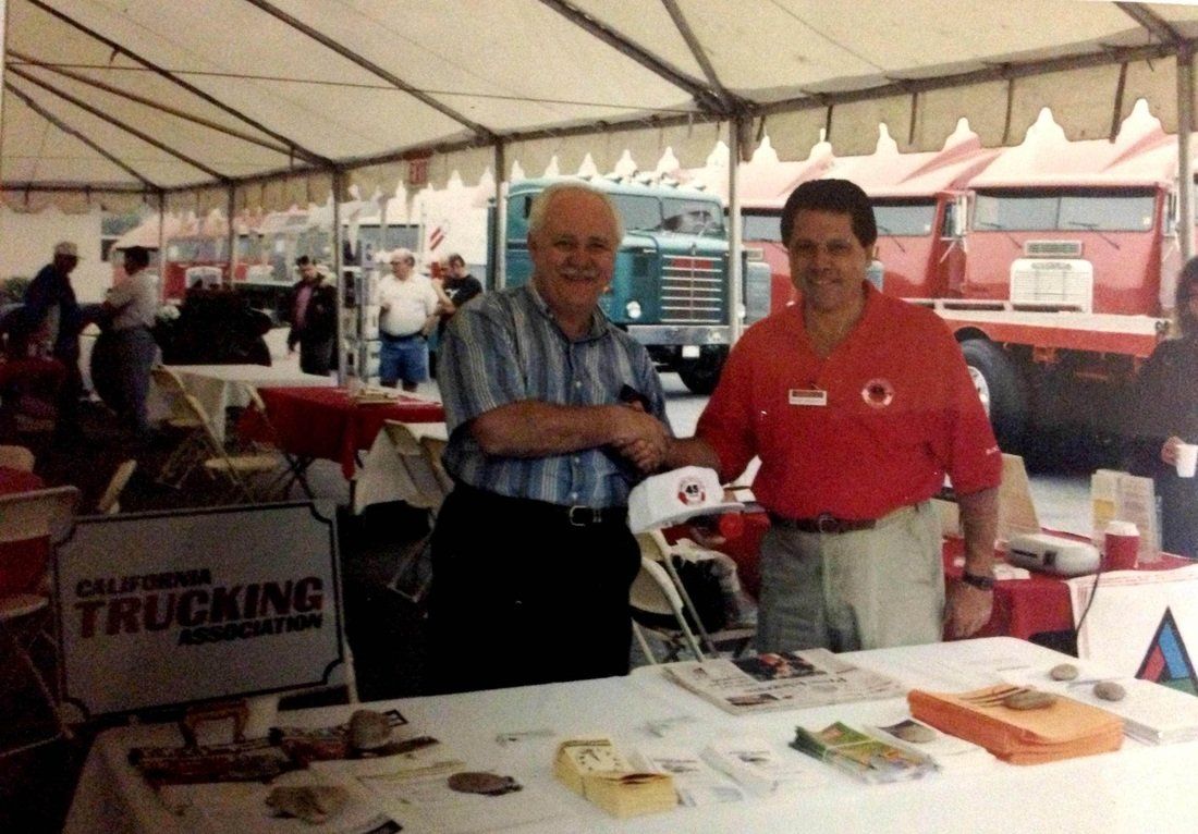Two men standing in front of a table that says california trucking