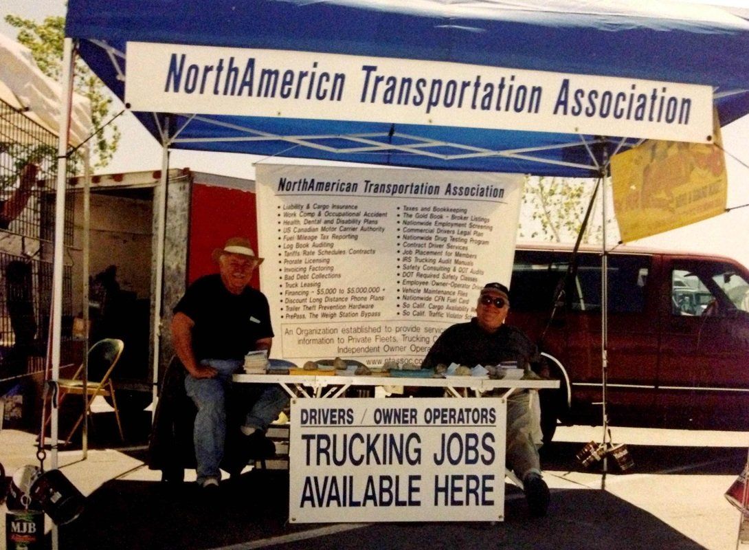 Two men sit under a north american transportation association tent