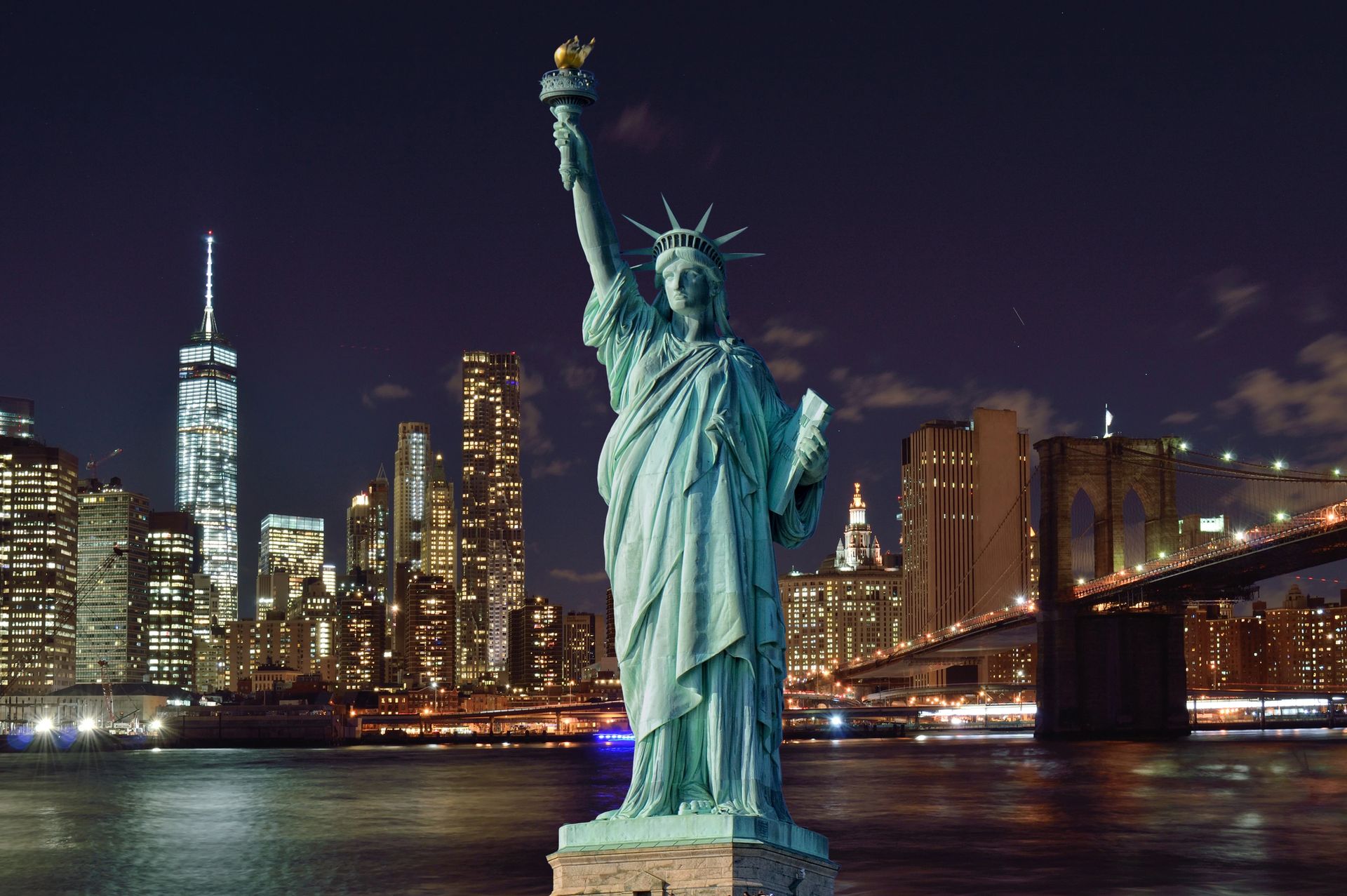 The statue of liberty is standing in front of a city skyline at night.