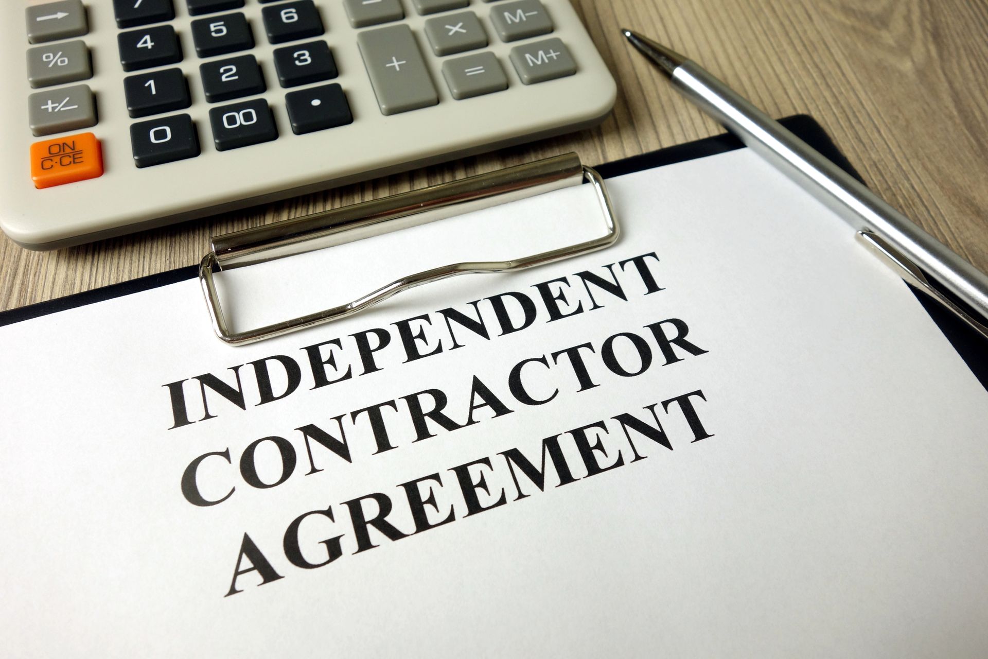 An independent contractor agreement is on a clipboard next to a calculator and pen.