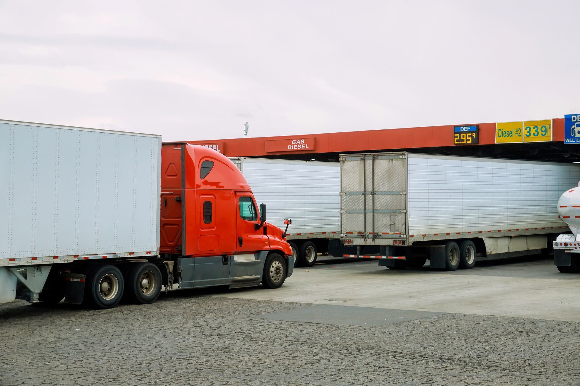 4 semi trucks are parked next to each other at a fuel island.