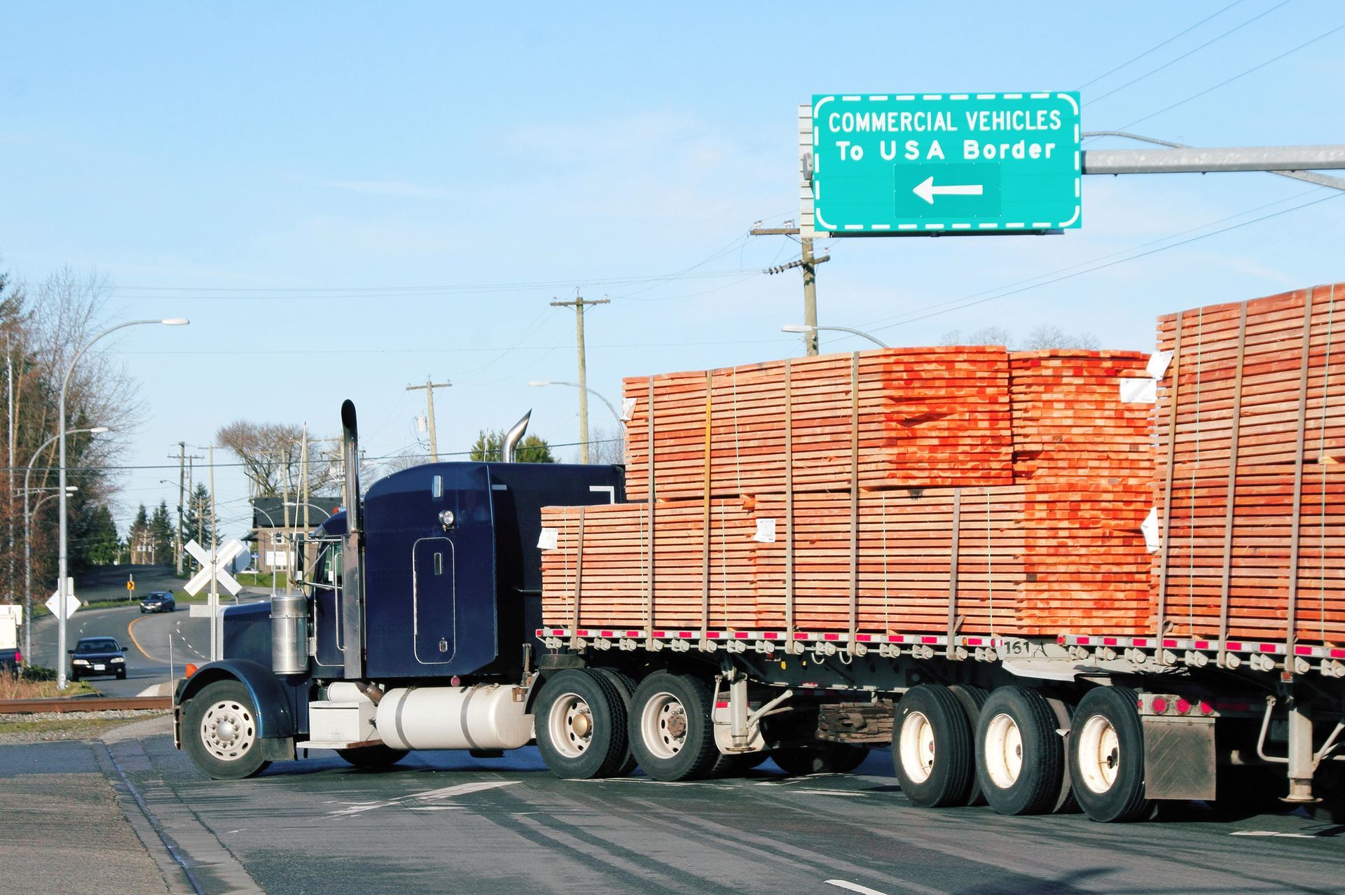 A truck is carrying a load of wood and a sign says commercial vehicles to usa border