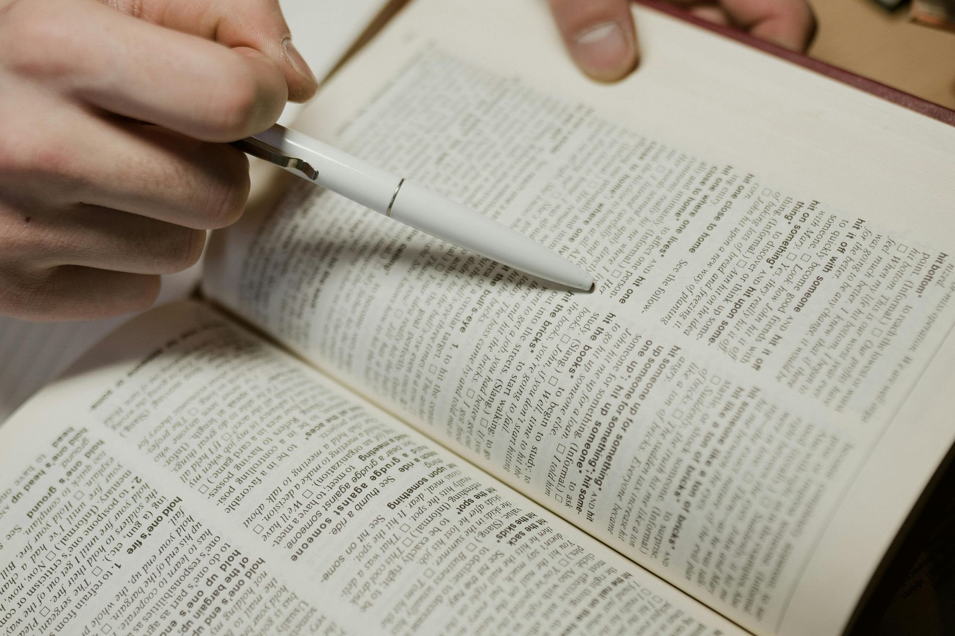 A person is writing in a dictionary with a pen.