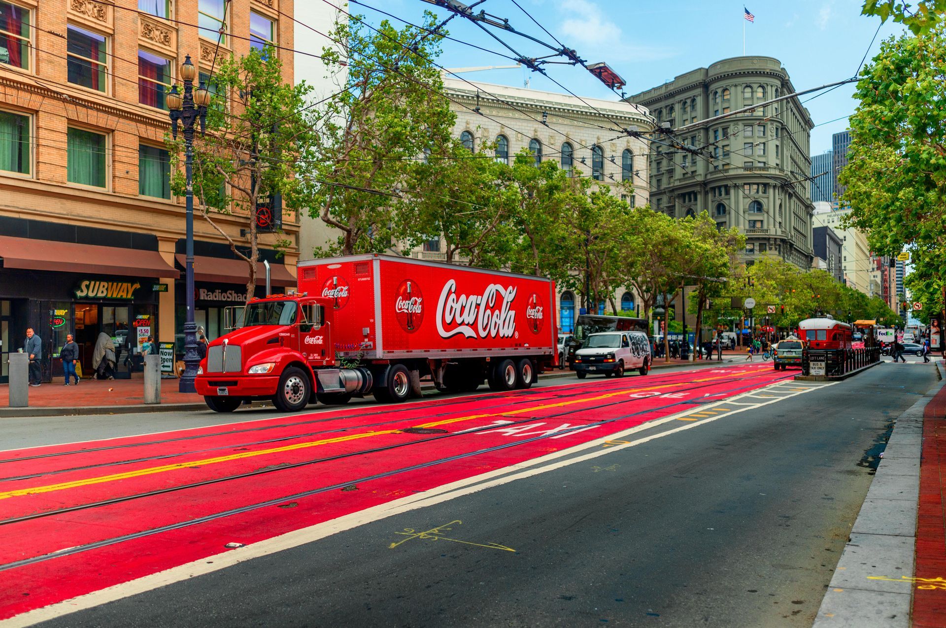 A red coca cola truck is driving down a city street