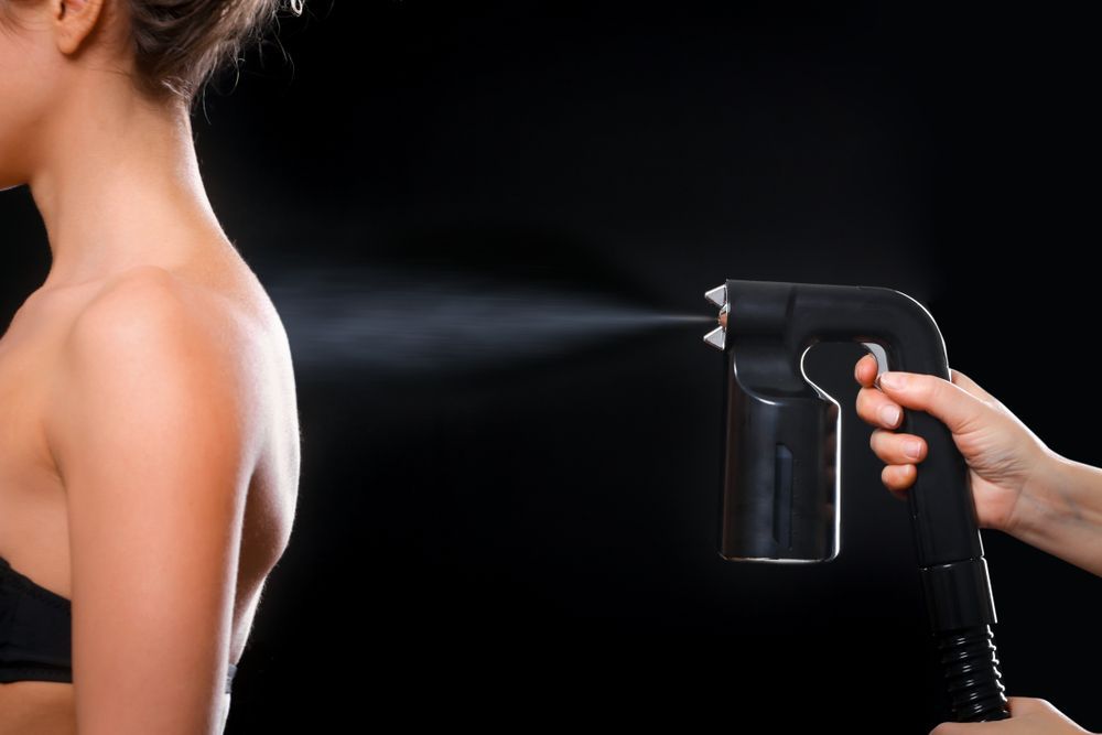 Person Receiving Spray Tan on Shoulder Against a Black Background — Aspire Beauty & Nails in Wagga Wagga, NSW